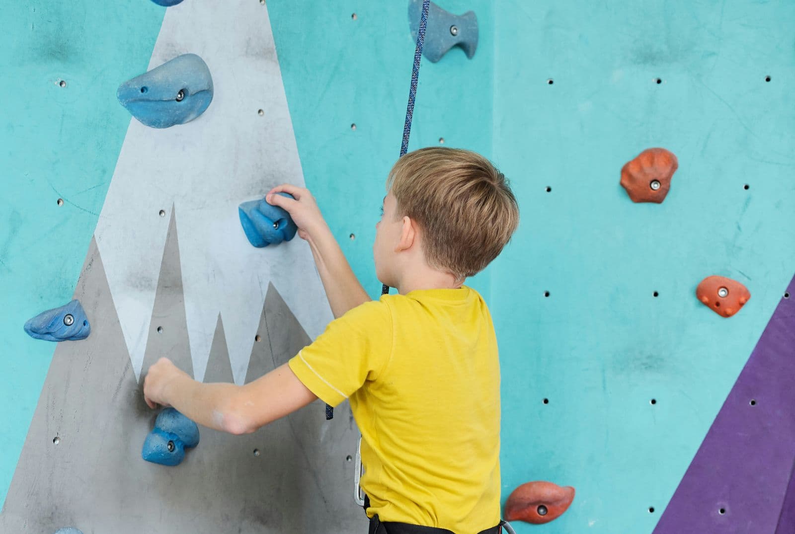 Enfant en t-shirt jaune attrapant une prise bleue sur un mur d’escalade
