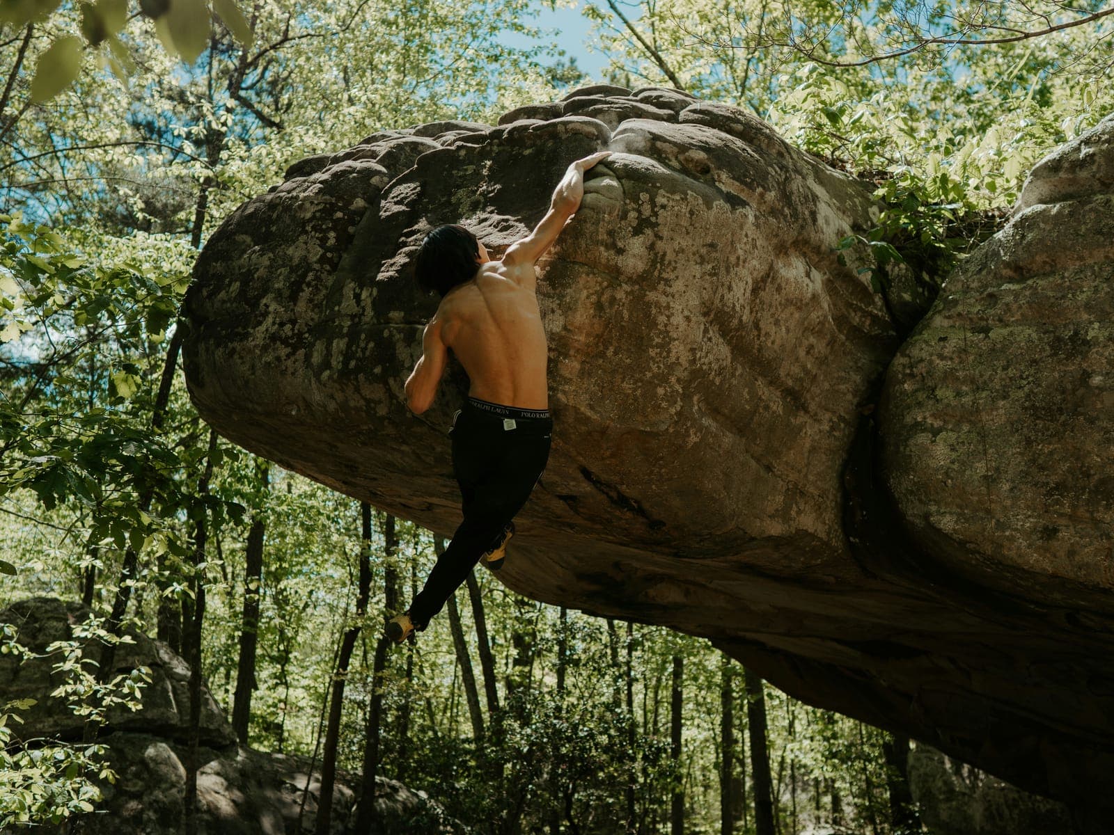 Grimpeur sous le dévers d’un rocher de grès en forêt