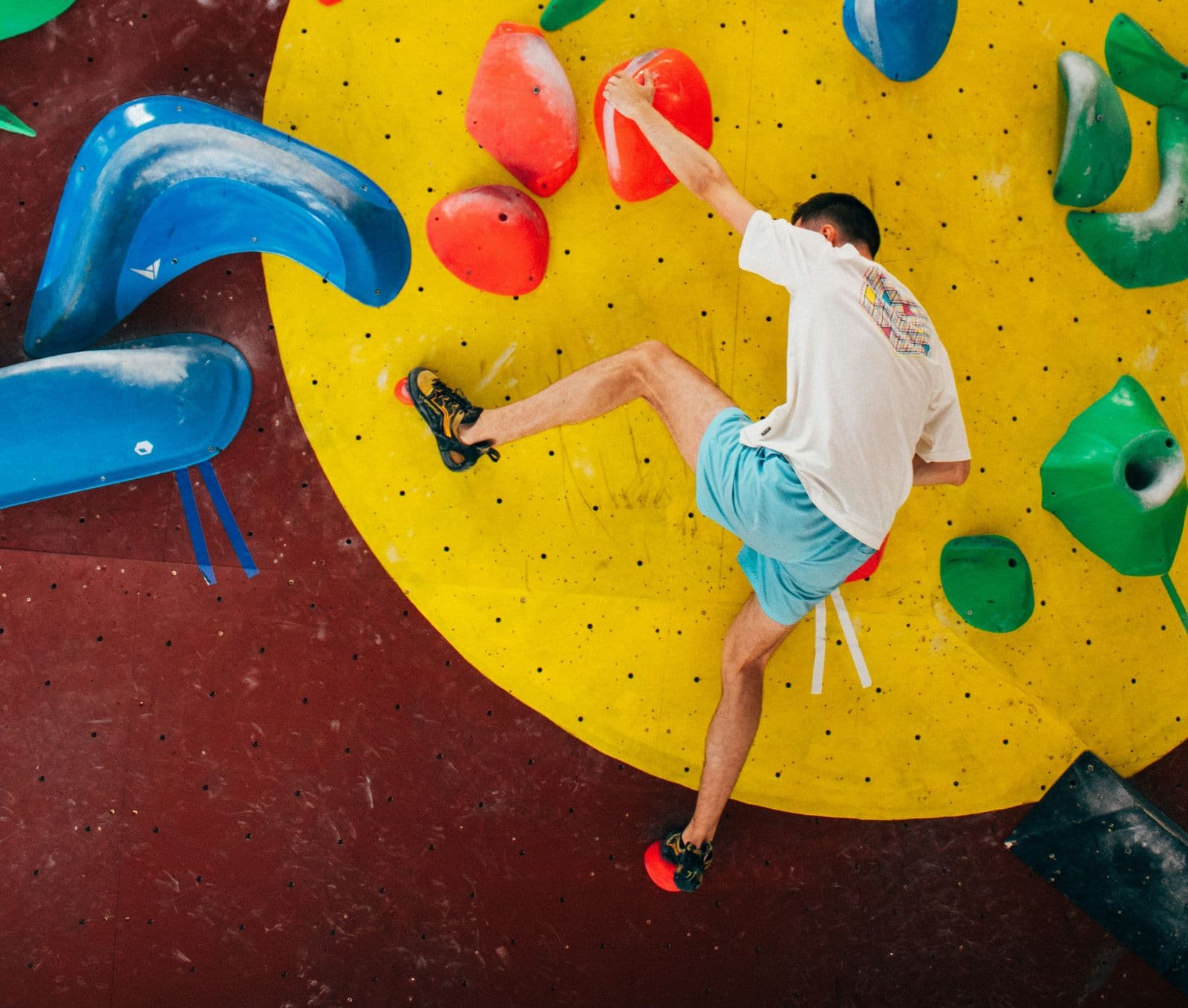Grimpeur vu de dessus sur un cercle jaune d’un mur de bloc aux prises colorées