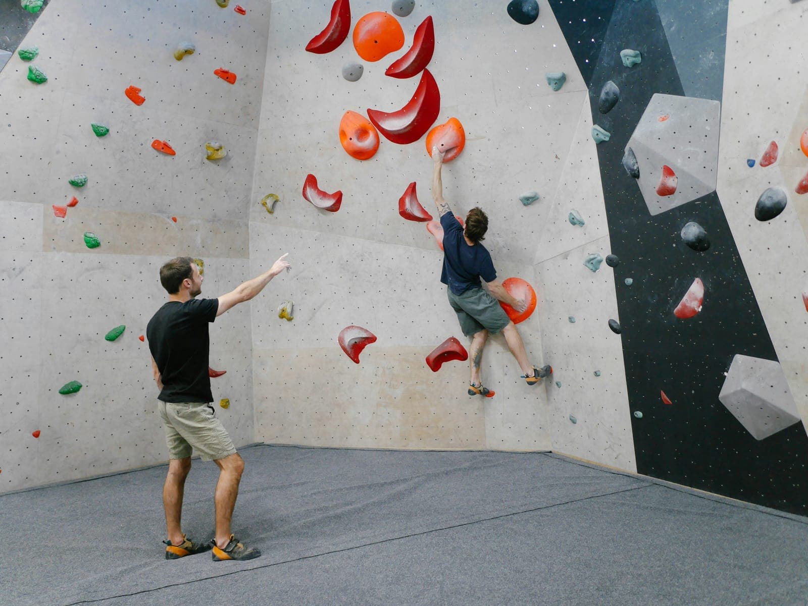 Grimpeur au pied du mur indiquant une prise à un autre grimpeur