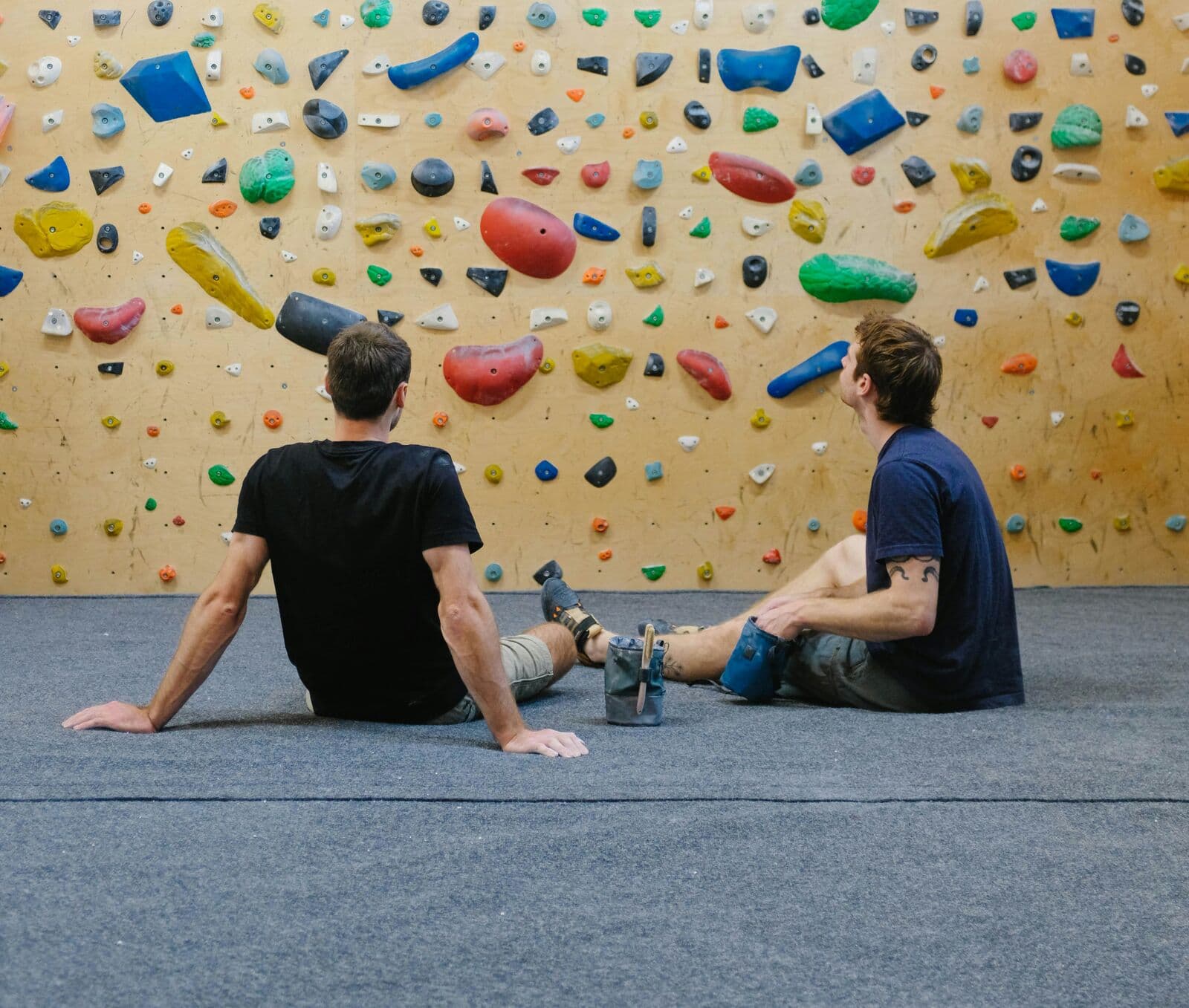 Deux grimpeurs assis sur le tapis face à un mur de bloc en bois